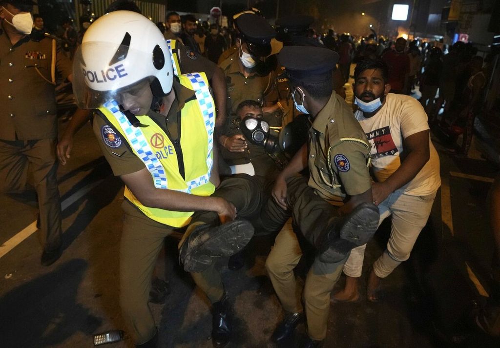 Sejumlah polisi Sri Lanka membawa seorang petugas yang terluka saat bentrokan dengan massa yang memprotes pemerintah terkait krisis ekonomi di luar kediaman pribadi presiden Sri Lanka di pinggiran Kolombo, Sri Lanka, Jumat (1/4/2022) dini hari. Seorang warga juga dilaporkan terluka terkena tembakan gas air mata. AP PHOTO/ERANGA JAYAWARDENA