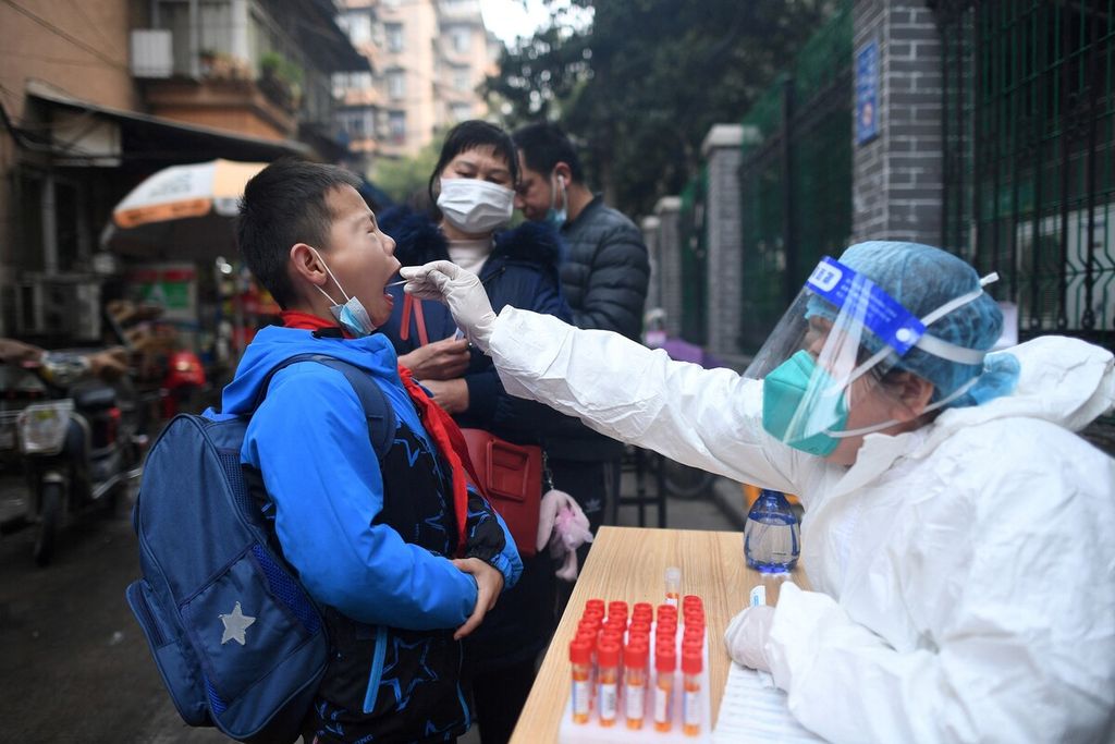 Seorang anak laki-laki membuka mulutnya lebar-lebar agar petugas bisa mengambil sampel untuk uji PCR di Wuhan, Provinsi Hubei, China, Jumat (4/3/2022).