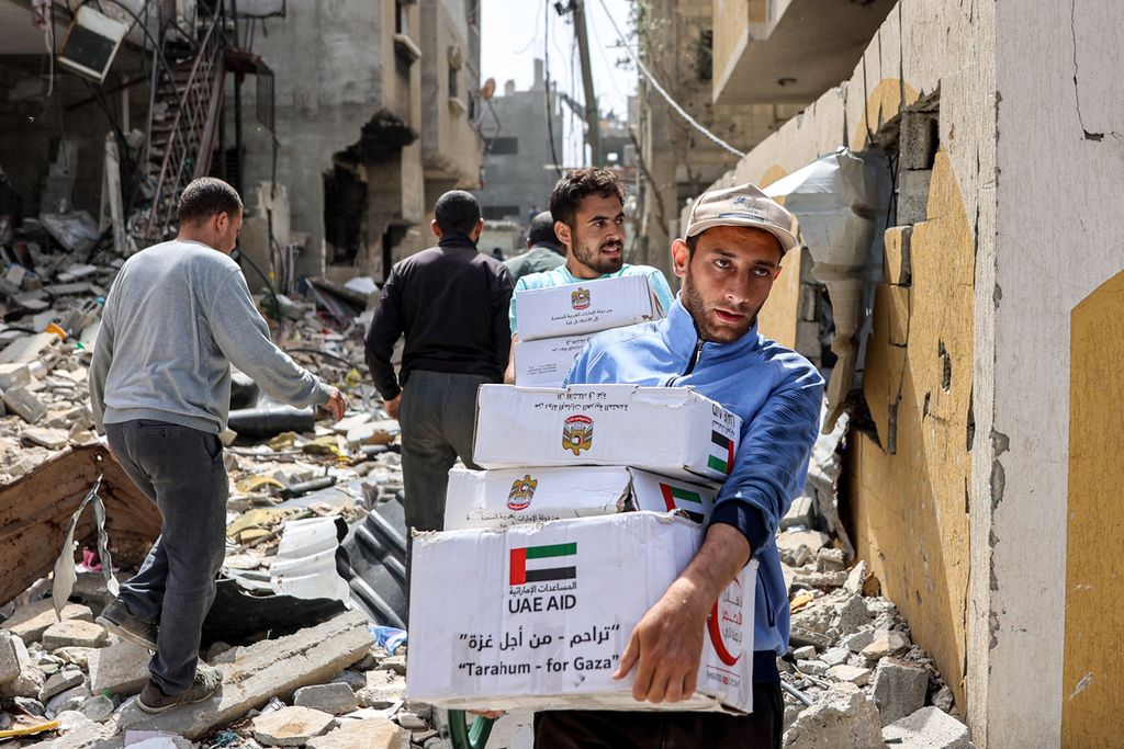 Warga Gaza, Palestina, membawa paket bantuan sosial melewati puing-puing bekas serangan Israel, 23 April 2024.
