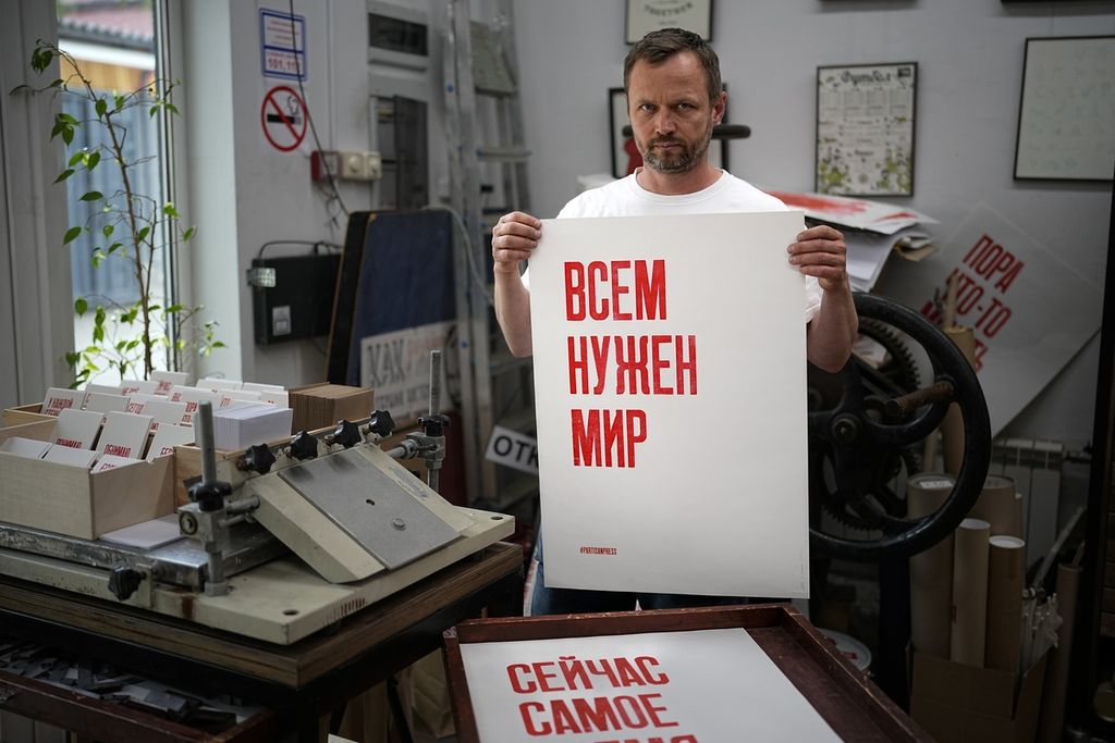 Sergei Besov, seorang seniman yang tinggal di Moskwa, Selasa (5/7/2022), memperlihatkan sebuah poster yang berisi pesan antiperang yang berbunyi  "Semua menginginkan perdamaian" yang dibuat di bengkel seni miliknya. 