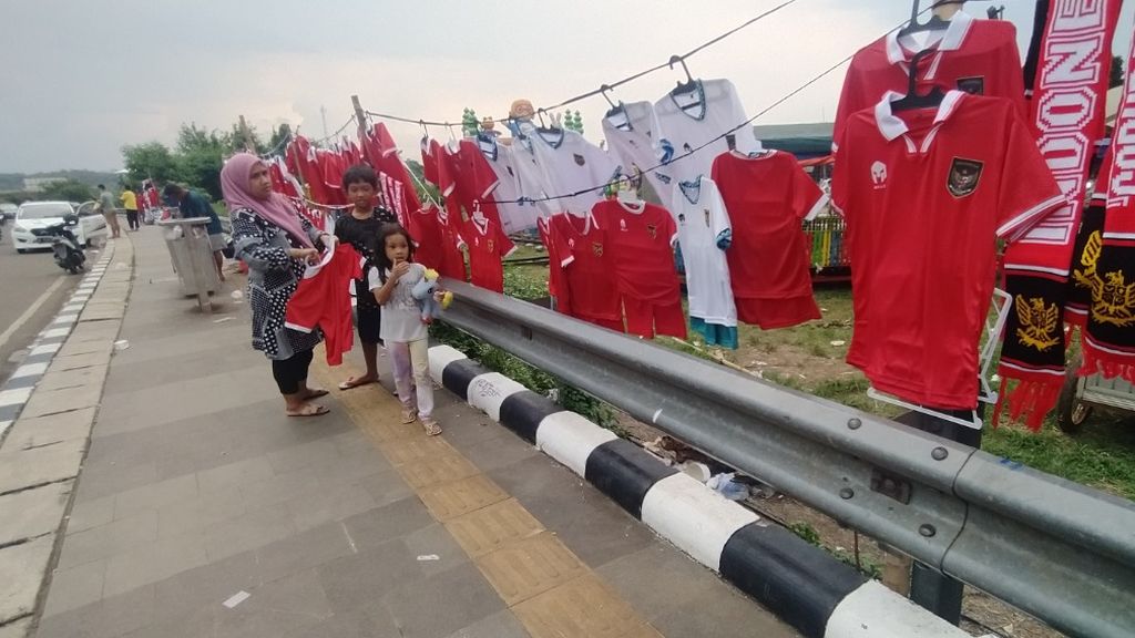 Aprilia (38) tengah membelikan kaos sepak bola timnas Indonesia untuk anaknya, Bentar (9) di lapak pedagang yang berada di sekitar Stadion Pakansari, Kabupaten Bogor, Jawa Barat, Minggu (9/10/2022).