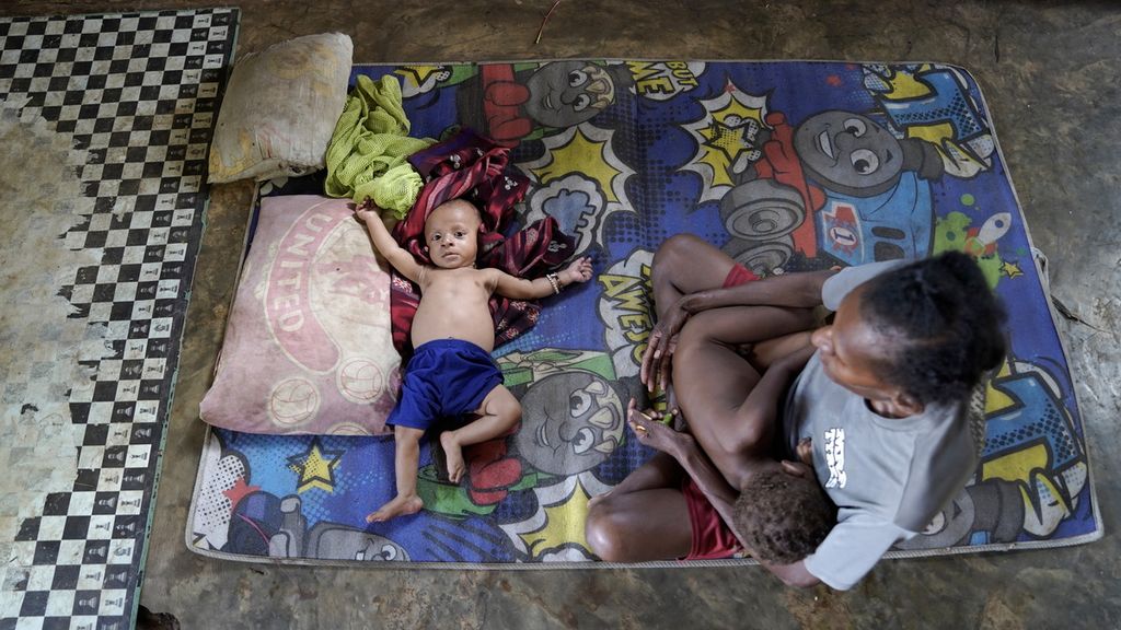 Demianus (6 bulan) tiduran tanpa baju di karpet tipis disamping ibunya Dorce Gebze (30) di Kampung Zanegi, Distrik Animha, Kabupaten Merauke, Papua, Kamis (10/11/2022). Bocah berusia enam bulan anak Kepala Kampung Zanegi ini terdata kekurangan gizi. 
