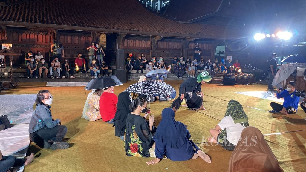Hujan turun saat pertunjukan berjudul <i>Legenda Godogan: Kungkum Kodok</i> dipentaskan di Bentara Budaya Jakarta, Jakarta, Sabtu (27/8/2022) malam. Sejumlah penonton berteduh di pinggir area pentas, sementara sebagian orang memilih bertahan dengan payung. Pentas tetap berlangsung meski hujan.