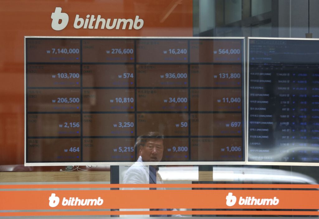 Refleksi seorang pria berjalan di depan papan yang menunjukkan harga bitcoin dan aset-aset kripto di pertukaran Bithumb di Seoul, Korea Selatan, pada 20 Juni 2018. 