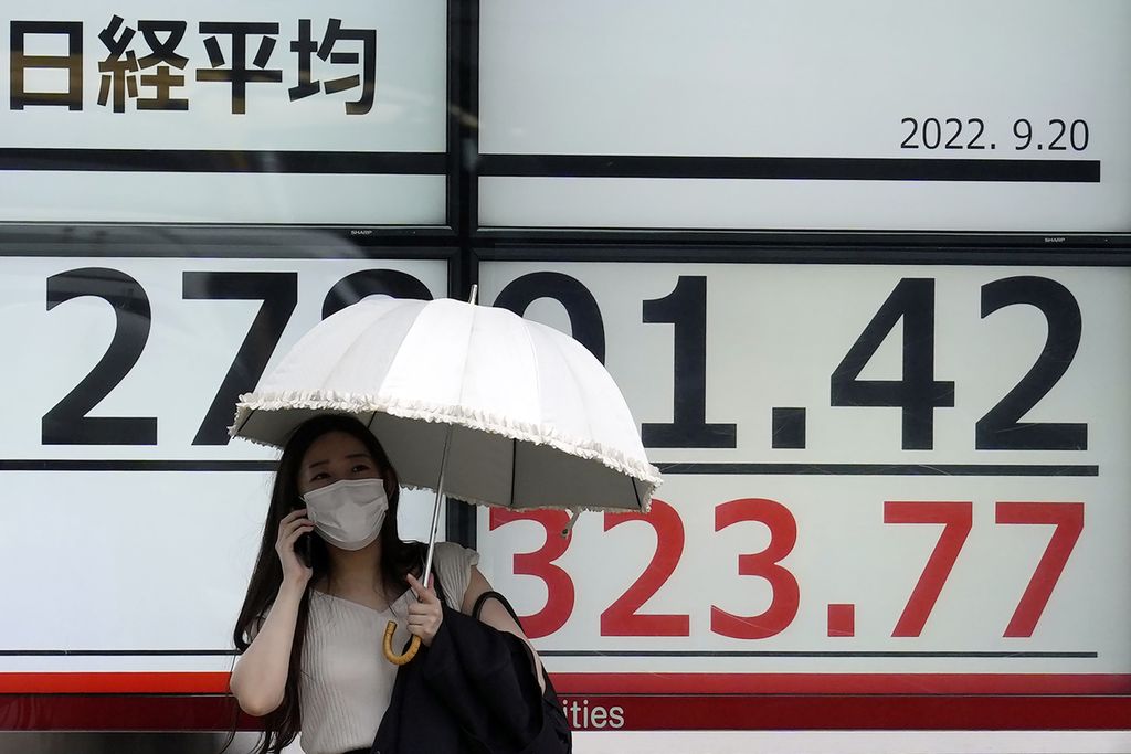 Seorang warga menggunakan payung sat berdiri di depan papan bursa elektronik yang menayangkan indeks Nikkei 225 di sebuah perusahaan sekuritas di Tokyo, Jepang, 20 September 2022. 