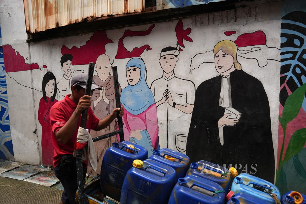 Penjual air bersih melintas di depan mural keberagaman dan kedamaian di Kelurahan Semper Barat, Cilincing, Jakarta Utara, Jumat (15/3/2024). 
