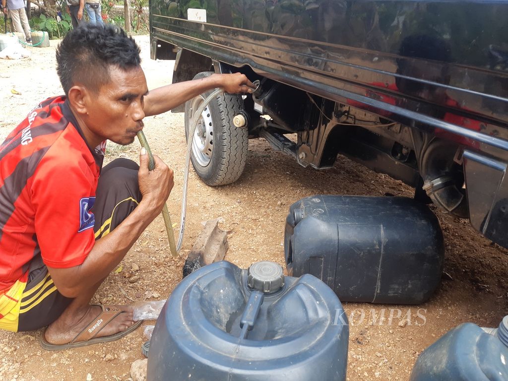 Seorang warga menyedot bahan bakar minyak dari dalam tangki mobil ia parkir di balik tembok SPBU di Desa Anakaka, Kecamatan Kodi, Kabupaten Sumba Barat Daya, Nusa Tenggara Timur, Rabu (23/8/2023). Kapasitas tangki itu lebih kurang 40 liter.