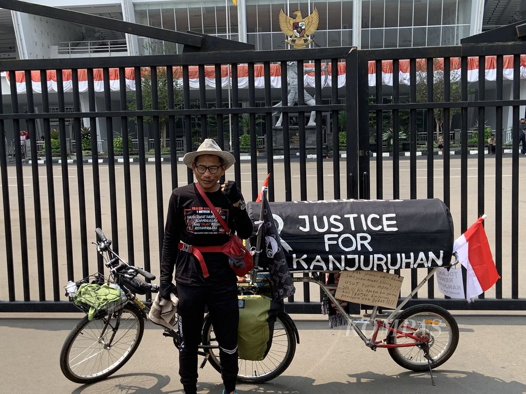 Miftahuddin Ramli (52) berfoto di depan area pintu masuk VIP Stadion Utama Gelora Bung Karno, Jakarta, Senin (14/8/2023) siang, sambil menuntun sepeda dengan keranda hitam di bagian belakang. Ia menyinggahi stadion di setiap kota selama perjalanan mengayuh sepeda dari Malang ke Jakarta untuk mengingatkan khalayak bahwa Tragedi Kanjuruhan belum selesai