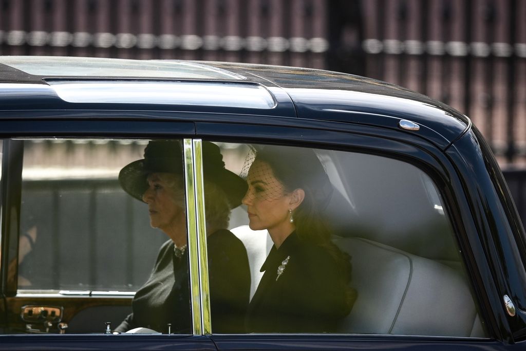 Istri Raja Charles III, Camilla, Queen Consort (kiri) dan Kate, Putri Wales, naik kendaraan di belakang iring-iringan pengantar peti jenazah Ratu  Elizabeth II dari Istana Buckingham ke Westminster Hall di London, Inggris, rabu (14/9/2022). 