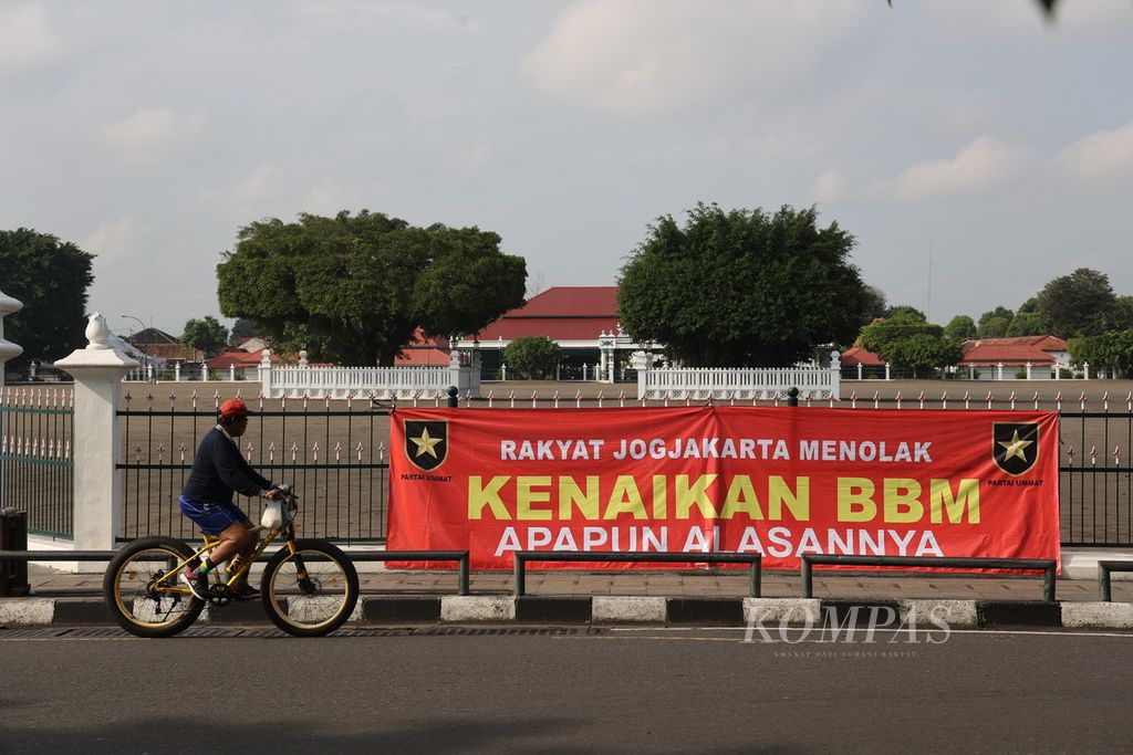 Pesepeda melintas di dekat spanduk berisi tulisan penolakan kenaikan harga BBM yang dipasang di pagar Alun-alun Utara, Yogyakarta, Sabtu (10/9/2022). Seruan penolakan kenaikan harga BBM masih gencar dilakukan oleh sejumlah kalangan masyarakat.