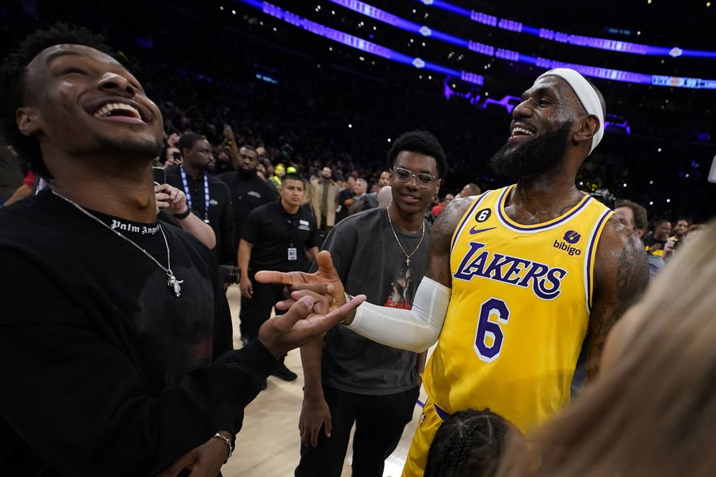Megabintang Los Angeles Lakers, LeBron James (kanan) bersenda gurau dengan anaknya, Bronny, saat Lakers menghadapi Oklahoma City Thunder pada lanjutan NBA, Rabu (8/2/2023) di Los Angeles, Amerika Serikat. James menumbangkan rekor Kareem Abdul-Jabbar sebagai pencetak poin terbanyak sepanjang masa NBA.