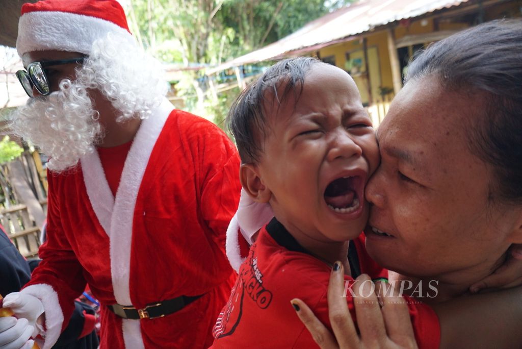 Azrakal (3) menangis dalam dekapan neneknya, Meydi Lengkong (44) ketika sekelompok sinterklas dan piet hitam dari Panitia Santa Claus God Bless berkunjung ke rumahnya di bilangan Paal IV, Manado, Sulawesi Utara, Sabtu (10/12/2022). Orangtua Azrakal membayar kelompok tersebut Rp 50.000 untuk memberi hadiah baginya.