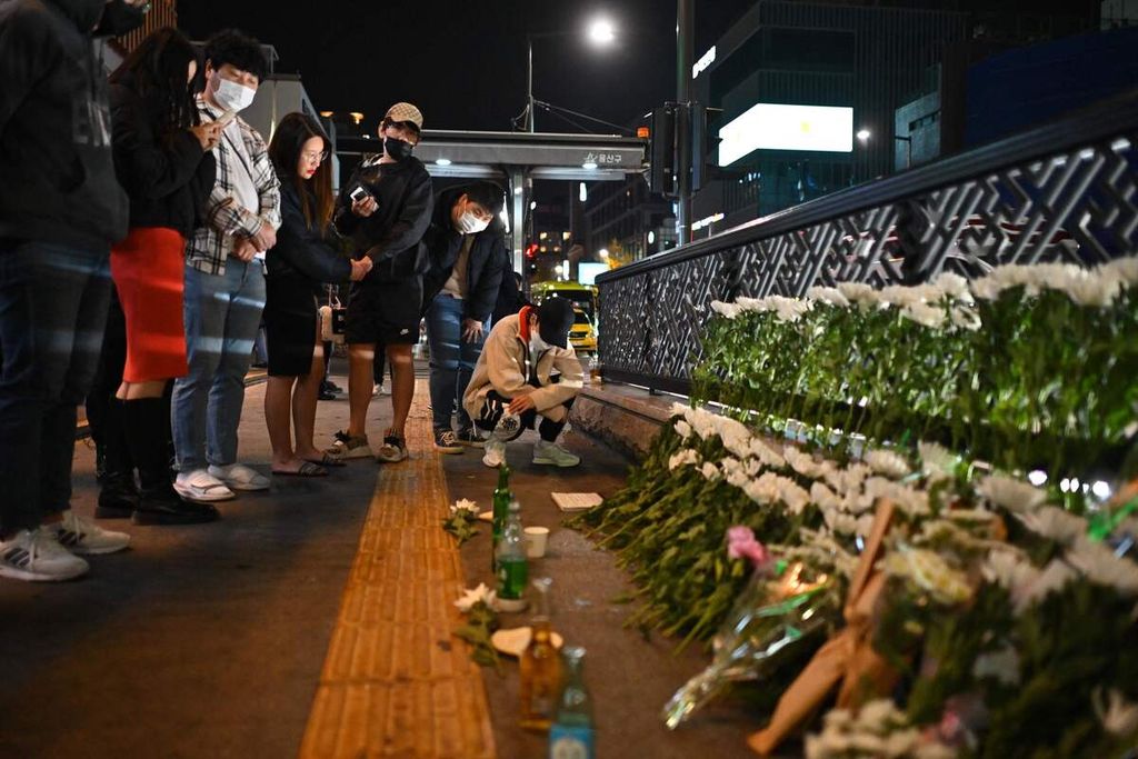 Orang-orang memperhatikan bunga-bunga yang diletakkan untuk mengenang korban Tragedi Itaewon di Stasiun Itaewon, Seoul, Minggu (30/10/2022). 