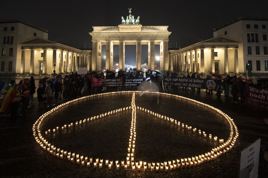 Warga Jerman menyalakan lilin dengan membentuk tanda perdamaian di depan Gerbang Brandenburg, Berlin, guna memperingati satu tahun Rusia menginvasi Ukraina, 23 Februari 2023.  