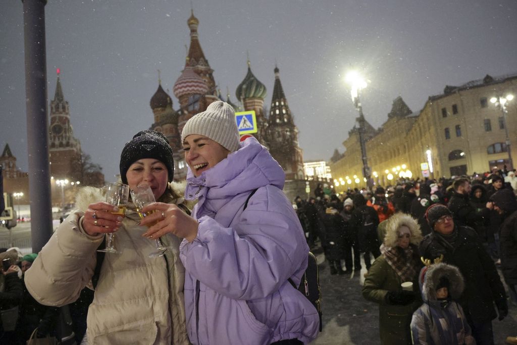 Dua warga bersulang <i>wine</i> di dekat Lapangan Merah, dengan pemandangan latar Katedral Santo Basilia dan Menara Spasskaya Tower selepas tengah malam di Moskwa, Rusia, Senin (1/1/2024). 