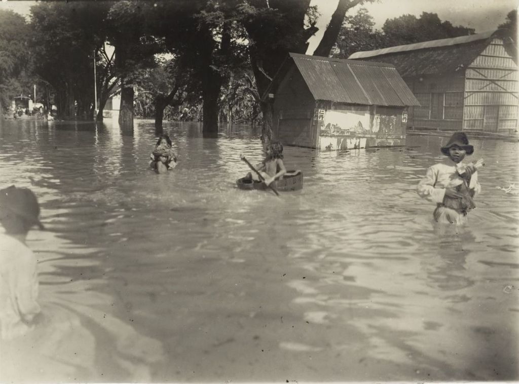 Anak-anak Bumiputra bermain di tengah banjir di sebuah kota di Hindia-Belanda sekitar tahun 1920. (Sumber: KITLV Leiden) 