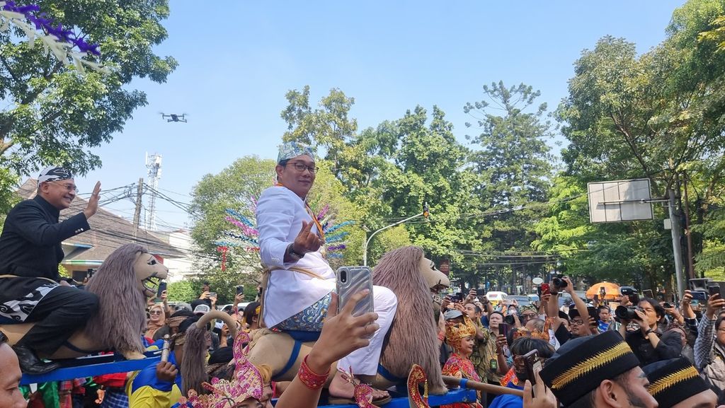 Gubernur Jawa Barat Ridwan Kamil memberikan simbol cinta dari jari kepada warga yang menyapanya saat diarak dengan sisingaan dalam perayaan Hari Jadi Ke-78 Jabar di Jalan Diponegoro, Kota Bandung (19/8/2023).