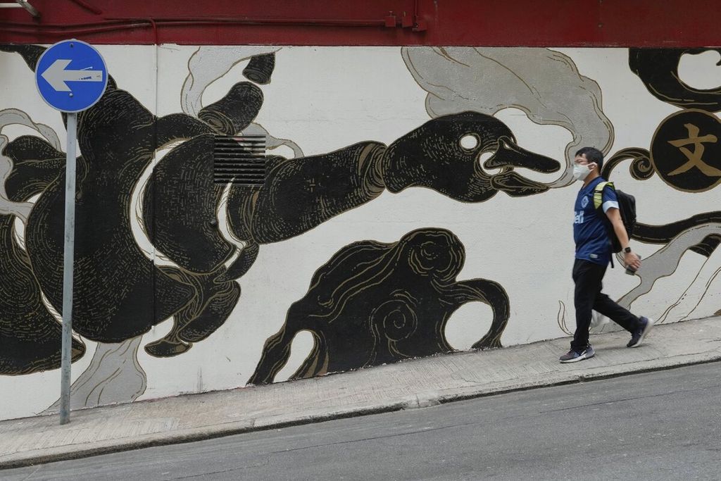 Warga berjalan melewati sebuah mural lukisan di salah satu kawasan pusat kota di Hong Kong, Senin (21/3/2022). Pelonggaran pembatasan juga akan meliputi pencabutan larangan makan di tempat do restoran setelah jam 6 sore dan pertemuan publik akan dibatasi pada empat orang setelah sebelumnya hanya dua orang. 