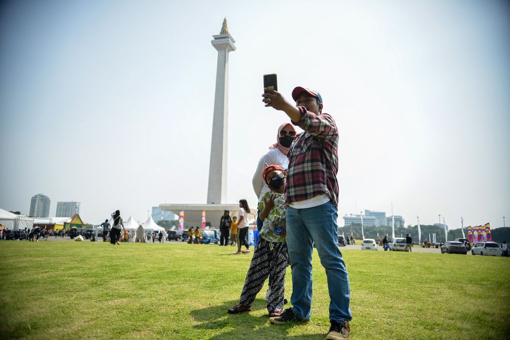 Satu keluarga foto bersama dengan latar belakang tugu Monumen Nasional (Monas), Jakarta, Minggu (21/5/2023).