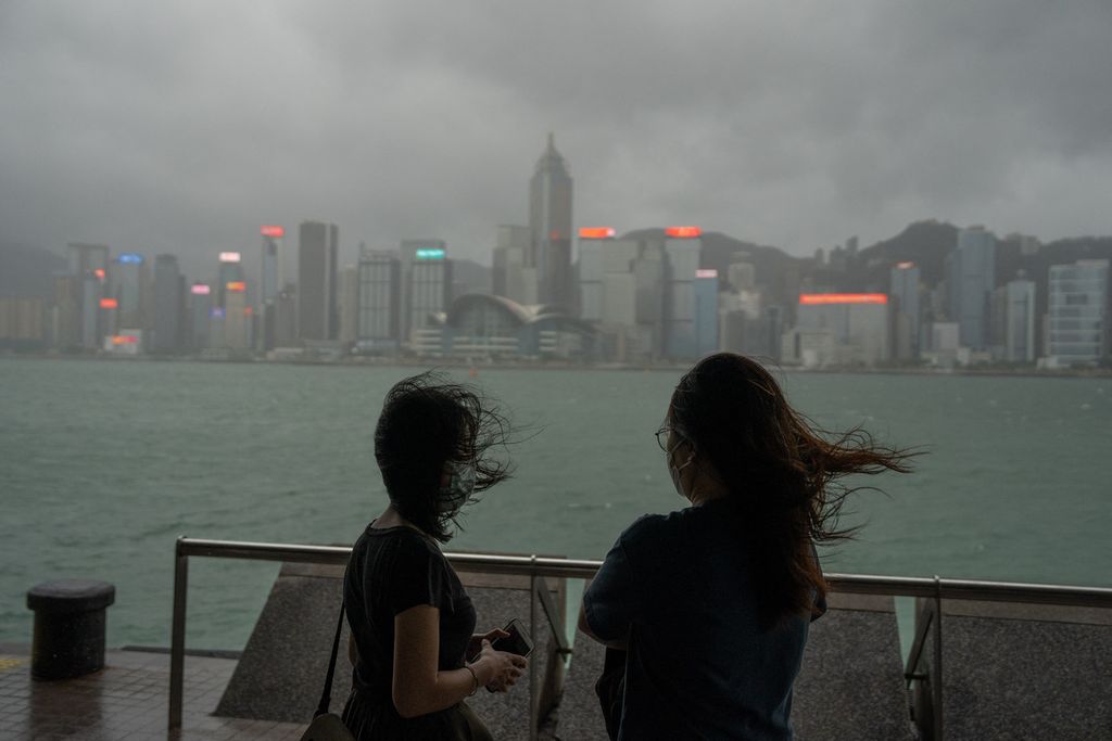 Dua orang berdiri di tengah terpaan angin kuat di jalanan tepi laut dekat Victoria Harbour saat topan Chaba melintasi Hong Kong, 2 Juli 2022. 