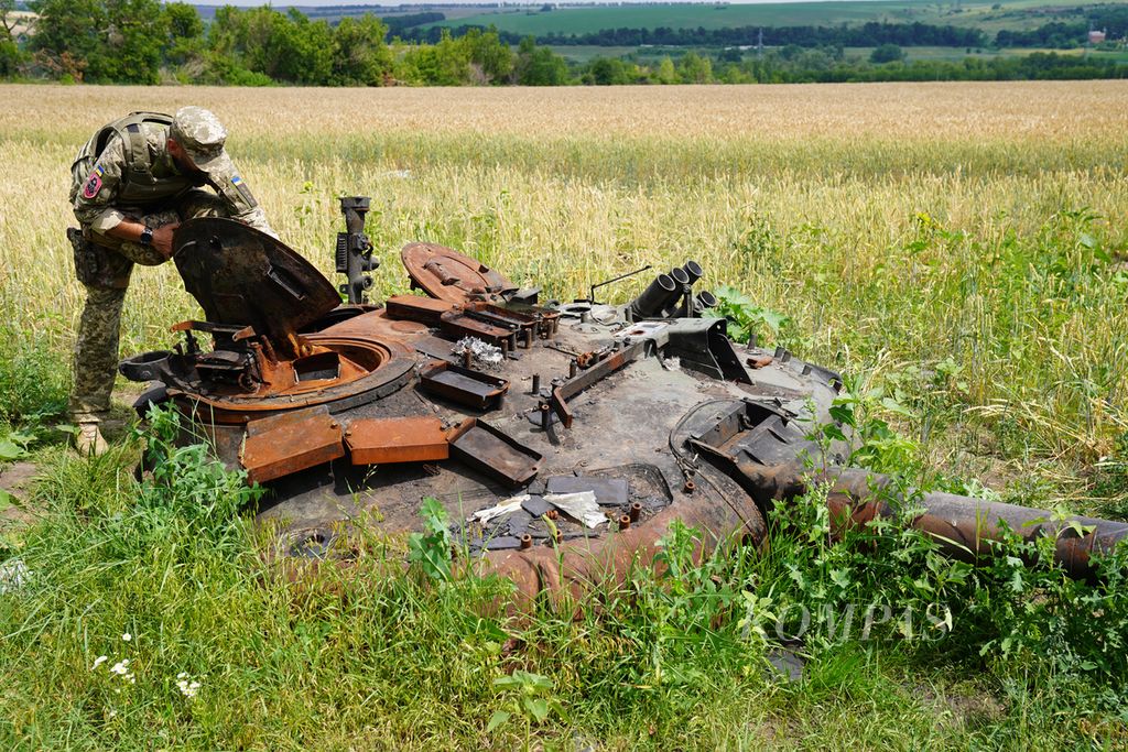 Anggota militer Ukraina memeriksa bagian tank milik Rusia yang hancur di sebuah ladang gandum di Desa Mala Rohan, Provinsi Kharkiv, Ukraina, Selasa (5/7/2022). Banyak ladang gandum di Ukraina yang masih tersebar bahan peledak dan ranjau yang belum dijinakkan. 