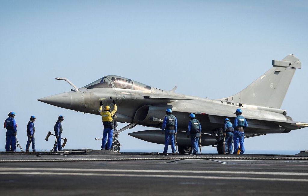 (FILES) This file photo taken on June 5, 2021 shows crew members standing next to a Rafale jet fighter on the deck of the French aircraft carrier Charles-de-Gaulle, off the coast of Toulon. - Indonesia on February 10, 2022 ordered 42 Rafale fighter jets from France, as Paris and Jakarta seek to strengthen military ties in the facing of growing tensions in the Asia-Pacific. 