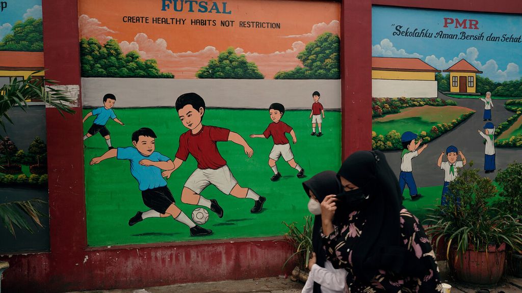 Warga melintasi mural yang menghiasai sebuah gedung sekolah dasar di Sukapura, Cilincing, Jakarta Utara, Senin (14/3/2022). Pembelajaran tatap muka atau PTM terbatas kembali didorong seiring perubahan level pemberlakuan pembatasan kegiatan masyarakat akibat pandemi Covid-19.