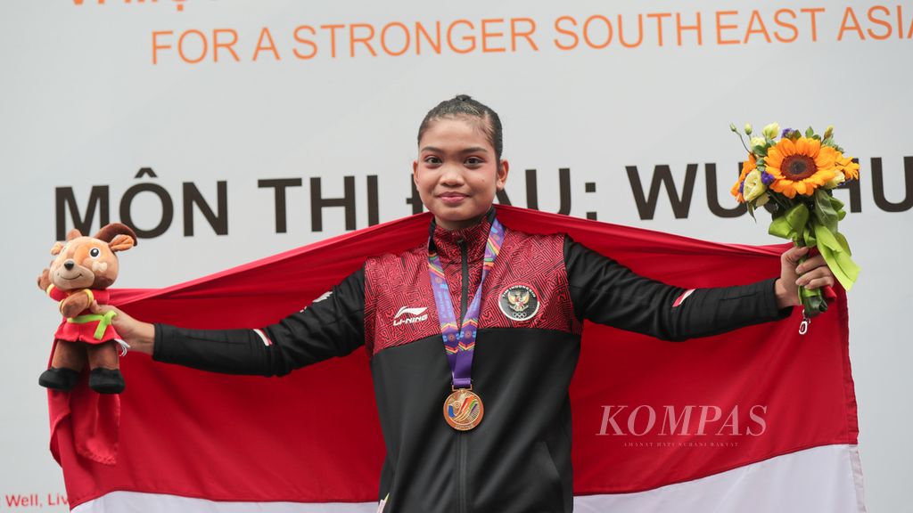 Atlet wushu Indonesia, Alisya Mellynar, mengibarkan bendera Merah Putih saat meraih medali emas nomor taijiquan cabang Wushu SEA Games Vietnam 2021 di Cau Giay Gymnasium, Hanoi, Vietnam, Sabtu (14/5/2022). Alisya merupakan debutan di SEA Games.