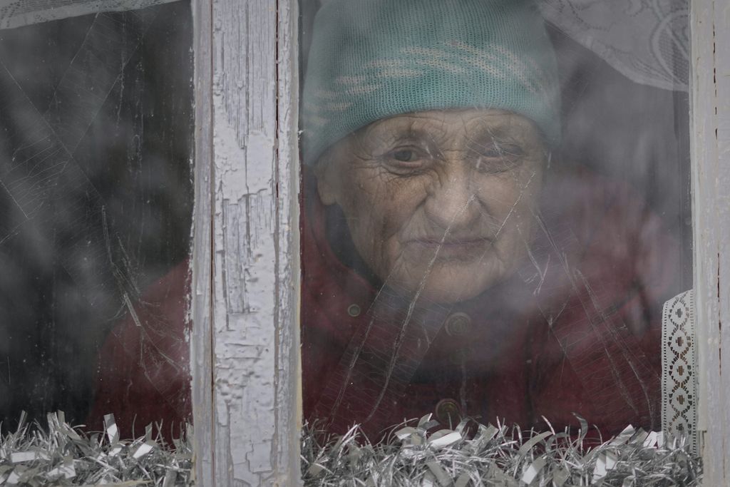 Anna Pylypivna menerawang keluar dari jendelanya di desa Novooleksandrivka, Ukraina, Senin (7/2/2022). Anna adalah salah seorang dari sedikit warga yang tak mau meninggalkan rumah mereka yang terletak di garis terdepan, berbatasan dengan Rusia, (AP Photo/Vadim Ghirda)