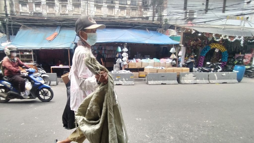 Seorang pemulung melintasi jalan kawasan Pasar Pagi Asemka, Kelurahan Pinangsia, Taman Sari, Jakarta Barat, Senin (21/11/2022), sembari melihat kondisi kios yang terbakar.