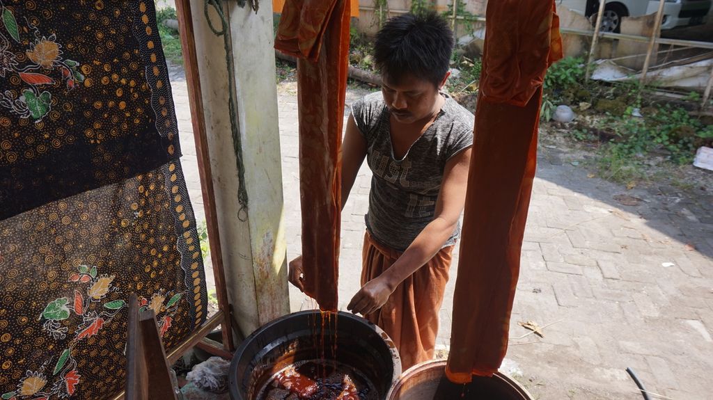 Abdul Mukib, pembatik, melanjutkan proses membatik dengan mencelupkan kain pada warna alam di rumah produksi batik tulis warna alam Mahkota, Bangkalan, Pulau Madura, Jawa Timur, Sabtu (23/7/2022). 