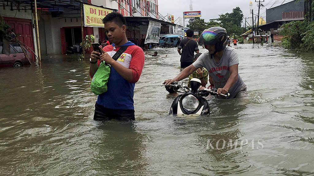 Warga mendorong  kendaraan roda dua saat melintas di Jalan Raya Paccerakkang di Kelurahan Paccerakkang, Biringkanaya, Kota Makassar, Sulawesi Selatan, Kamis (21/12). Banjir di wilayah ini merendam jalan dan permukiman dengan ketinggian air hingga  1,5 meter.