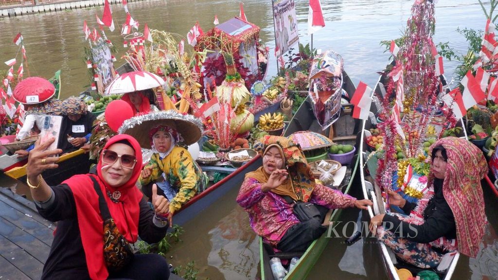  A female visitor (with a red hijab) takes a selfie with the floating market traders who gathered at the Banjarmasin Floating Market Pier, Monday (15/8/2022). They decorated their respective boats with red and white flags in order to welcome the 77th Anniversary of Indonesian Independence, as well as enliven the 72nd Anniversary of South Kalimantan Province.