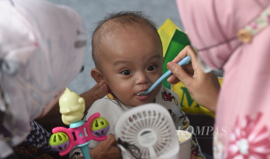 Ibu memberi makan bayinya dengan bubur sehat saat peluncuran Gebyar Lomba Balita Sehat di Halaman Balaikota Surabaya, Jawa Timur, Rabu (26/1/2022). 