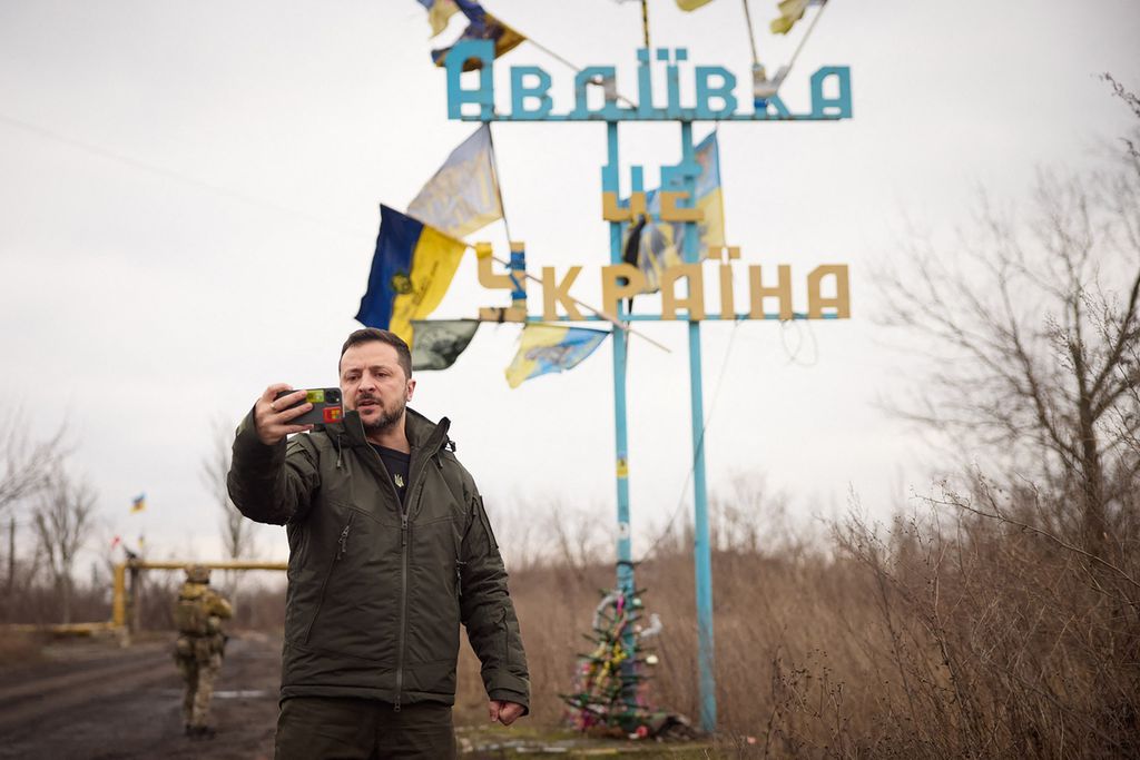 Presiden Ukraina Volodymyr Zelenskyy merekam pidato di depan papan bertuliskan ”Avdiivka adalah Ukraina” di kota Avdiivka, wilayah Donetsk, di tengah invasi Rusia ke Ukraina, Jumat (29/12/2023). 