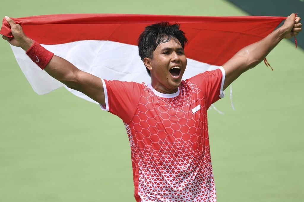 Muhammad Rifqi Fitriadi membawa bendera Merah Putih usai memastikan kemenangan tim Piala Davis Indoneia atas Venezuela pada babak <i>playoff </i>Grup II Piala Davis di Stadion Tenis Gelora Bung Karno, Jakarta, Sabtu (5/3/2022). 