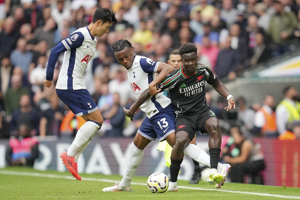 Pemain Tottenham Hotspur, Son Heung-min (kiri), berusaha membantu Destiny Udogie (tengah) untuk merebut bola dari pemain Arsenal, Bukayo Saka, pada laga Liga Inggris di London, Sabtu (15/9/2024). Arsenal memenangi laga dengan skor 1-0.