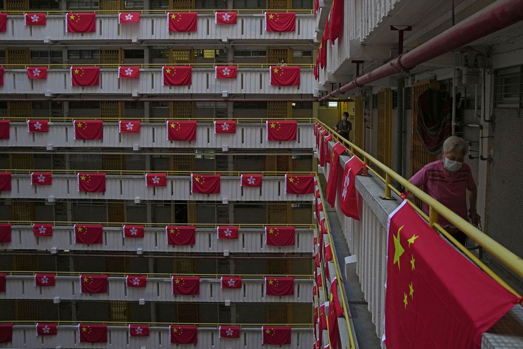 Warga berjalan di samping bendera China dan Hong Kong yang dipasang di sebuah kompleks apartemen untuk memperingati 25 tahun penyerahan Hong Kong dari Inggris kepada China, 1 Juli 2022, di Hong Kong. 