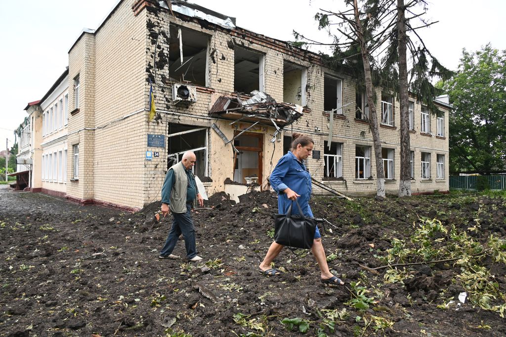 Dua warga melintas di depan gedung yang rusak sebagian akibat serangan militer Rusia di Chuguiv, sebelah timur Kota Kharkiv, Sabtu (16/7/2022). 