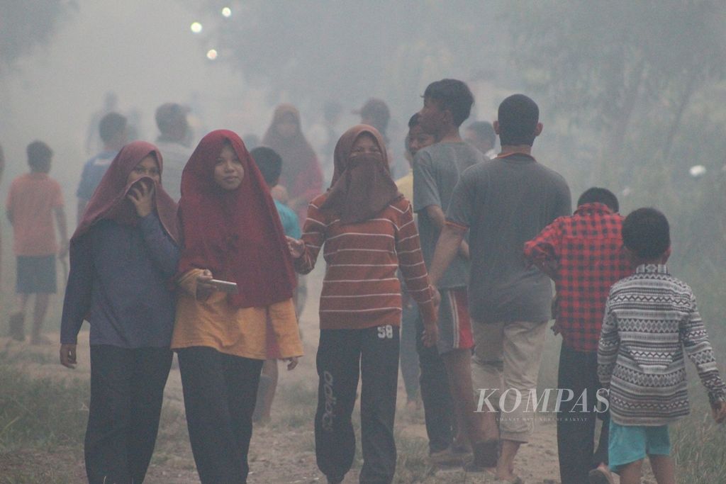 Warga melewati kepulan asap hasil kebakaran lahan di Kelurahan Sri Mulya, Kecamatan Sematang Borang, Kota Palembang, Sumatera Selatan, Selasa (15/10/2019). Api sudah mendekati rumah warga. Mereka pasrah karena air sudah sangat terbatas. Mereka sangat membutuhkan bantuan.