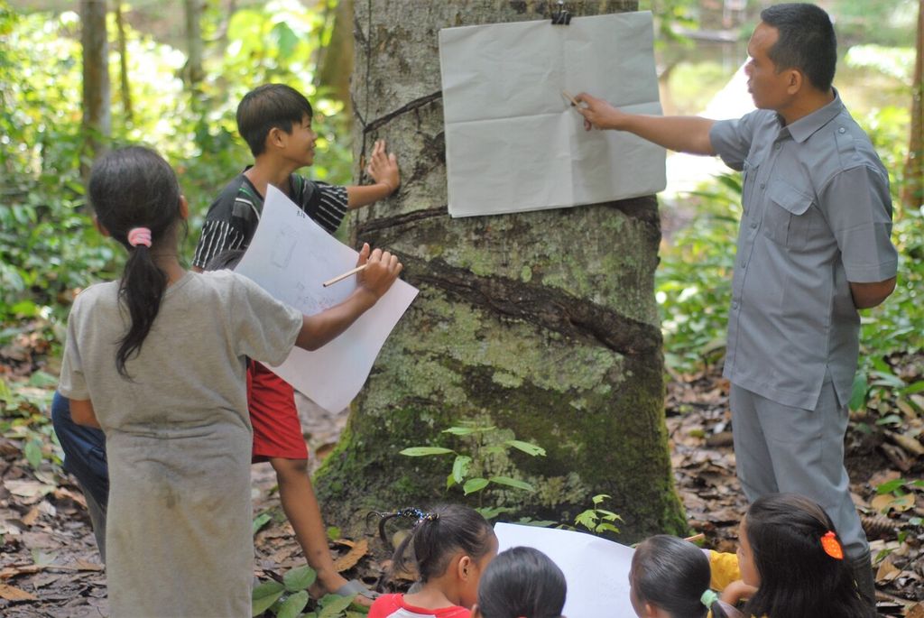 Teguh dan siswanya dari Suku Batin Sembilan di Hutan Harapan dalam kegiatan belajar mengajar di wilayah Kelompang, Kabupaten Batanghari, Jambi, Jumat (26/11/2021). Pendidikan adaptif terus dikembangkan demi menjangkau anak-anak di pedalaman. Guru mengambil peran penting di dalamnya.