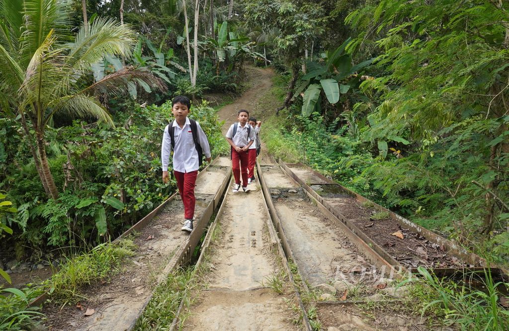 Siswa berjalan melewati jembatan yang rusak akibat tanah bergerak menuju Madrasah Ibtidaiyah Pasawahan, Kecamatan Banjaranyar, Kabupaten Ciamis, Jawa Barat, Selasa (19/7/2022). Mayoritas siswa berjalan kaki menuju sekolah selama lebih kurang 20 menit.