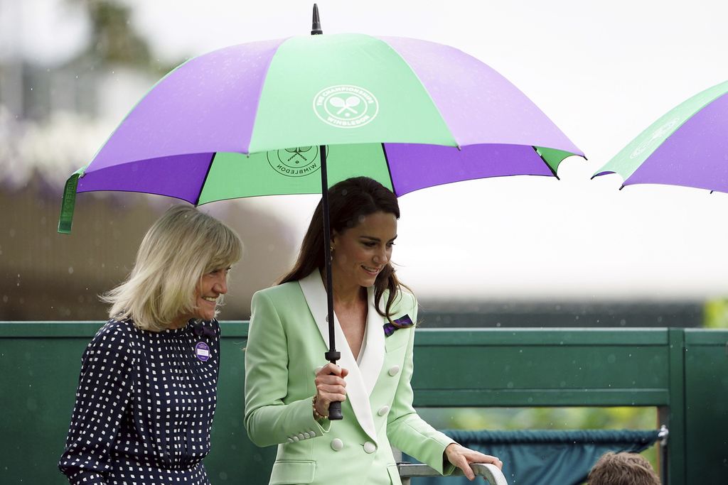 Putri Wales Kate Middleton bersama mantan petenis Debbie Jevans (kiri) menunggu redanya hujan di bawah payung untuk melihat pertandingan tunggal putri antara Katie Boulter melawan Daria Saville pada hari kedua kejuaraan tenis Wimbledon, Selasa (4/7/2023). Karena hujan, hanya ada 8 laga yang selesai dari 77 laga yang harusnya berlangsung pada hari itu. 