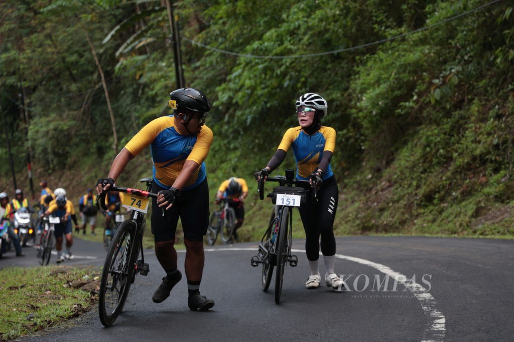 Para pabalap menuntun sepedanya saat melintasi tanjakan di Tamanjaya, Ciemas, Sukabumi, Jawa Barat pada etape pertama Cycling de Jabar 2023, Sabtu (8/7/2023). 