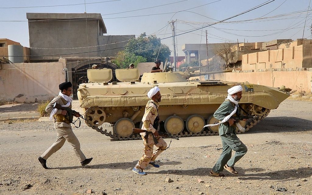 Anggota milisi Syiah, Hashed al-Shaabi, berlari di samping tank dalam serangan bersama pasukan Irak di Kota Hawija, Irak, Kamis (5/10). Militer Irak mengklaim telah merebut kota itu dari milisi Negara Islam di Irak dan Suriah (NIIS).