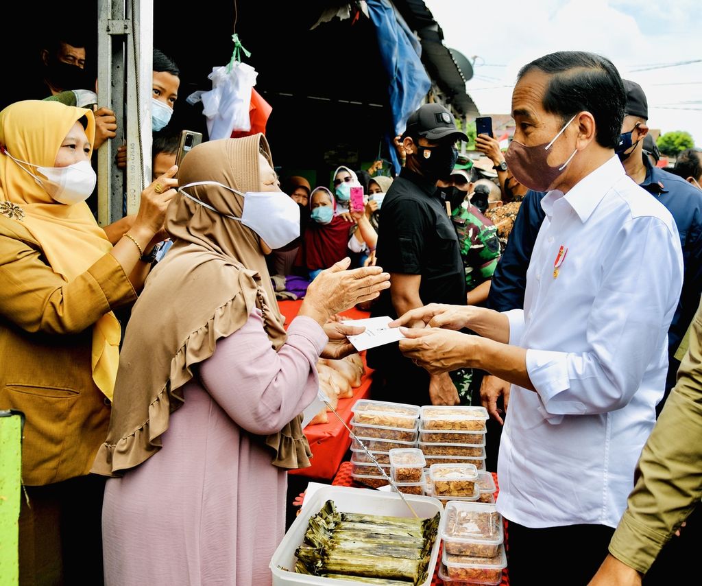Presiden Joko Widodo berbincang sembari menyerahkan bantuan tunai kepada pedagang di Pasar Tanjung Enim, Kabupaten Muara Enim, Sumatera Selatan, Senin (24/1/2022).