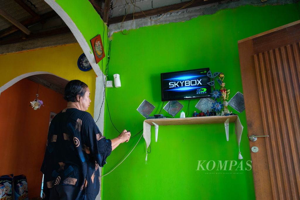 Zaitun menyalakan televisi menggunakan listrik tenaga surya di Pulau Mecan, Kota Batam, Kepulauan Riau, Selasa (12/12/2023).