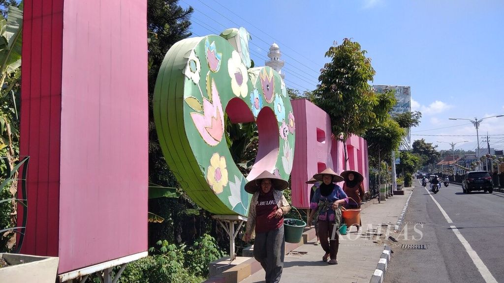 Tiga petani hortikultura berjalan di trotoar di depan tulisan "I Love Batu" di Kota Batu, Jawa Timur, Juni 2020.