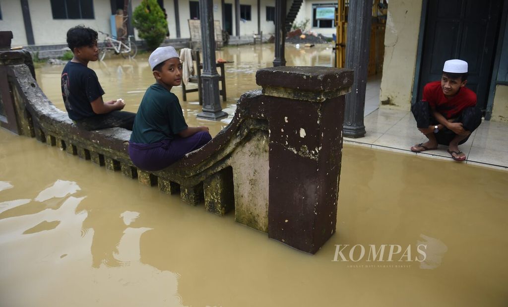 Santri Pondok Pesantren Al-Munawwir duduk di pagar pesantren saat banjir di Desa Blega, Kecamatan Blega, Kabupaten Sampang, Jawa Timur, Minggu (1/1/2023). 