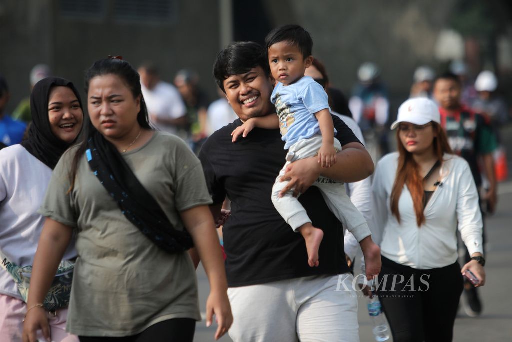 Seorang bapak tersenyum bersama istrinya saat menggendong anaknya jalan-jalan di kawasan bebas kendaraan bermotor di Jakarta, Minggu (28/5/2023). 